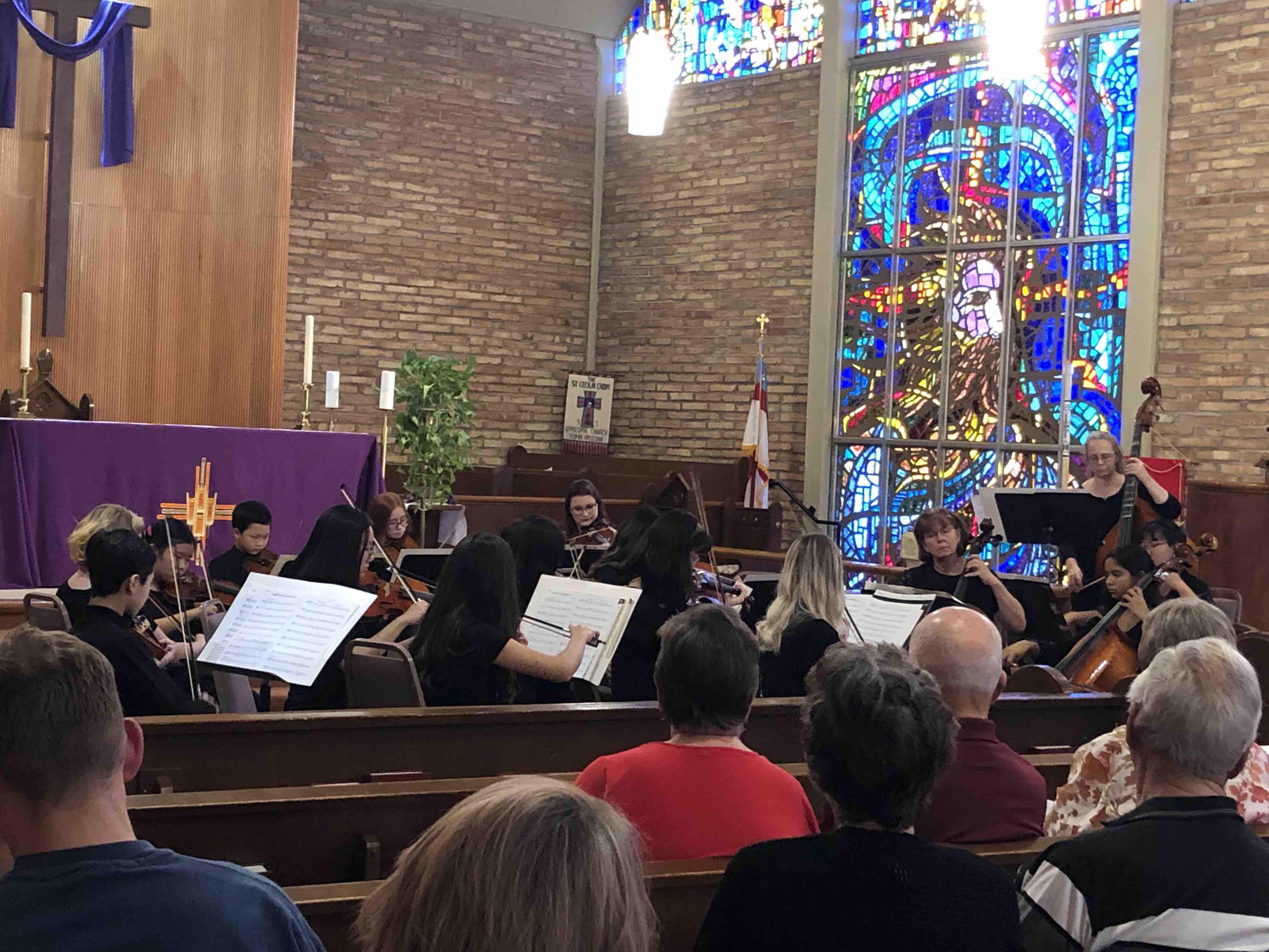 Audience members sit in the rows of a large church with stained-glass windows.