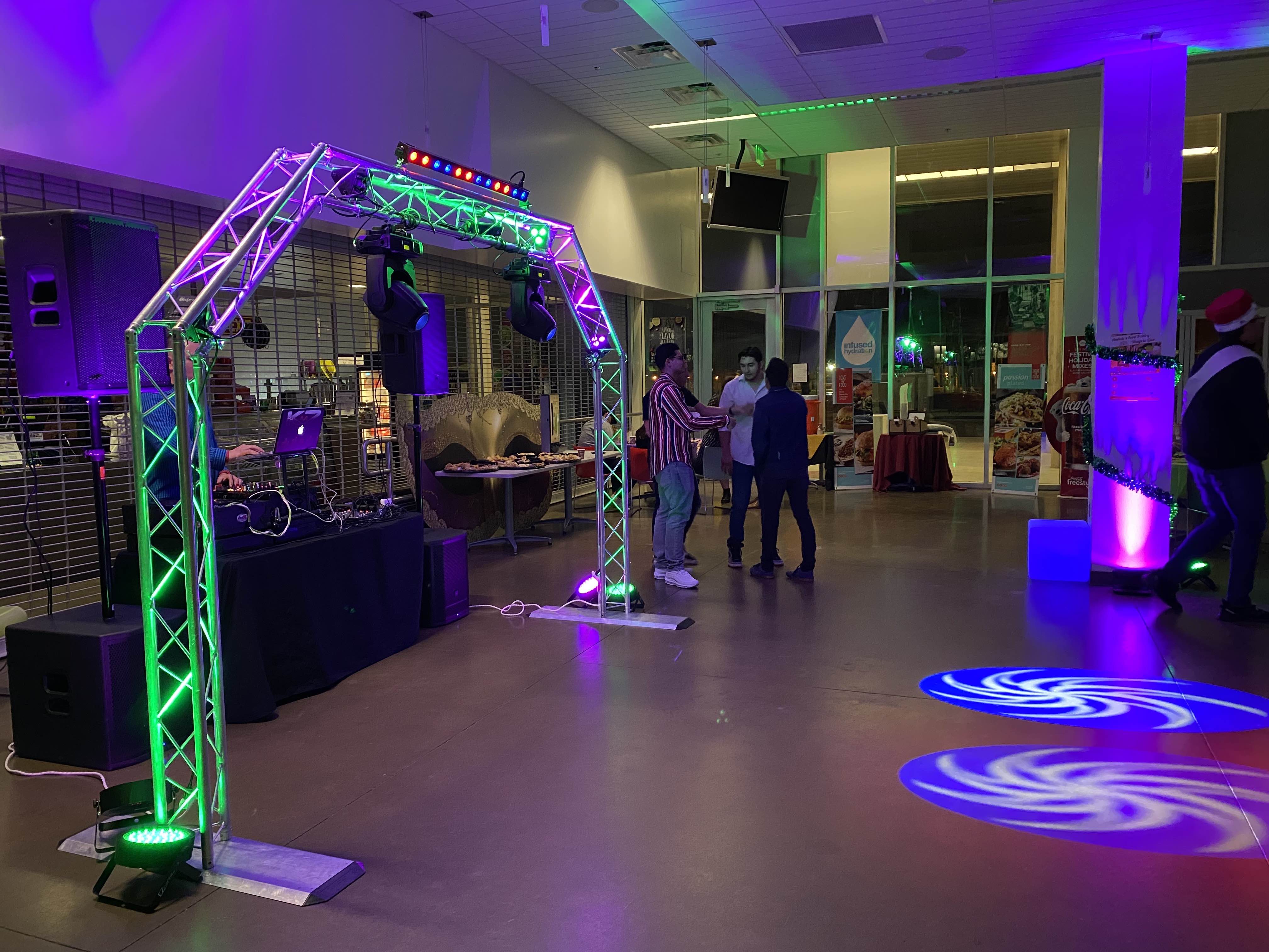 people stand in a colorfully lit (purple and green) cafeteria party.