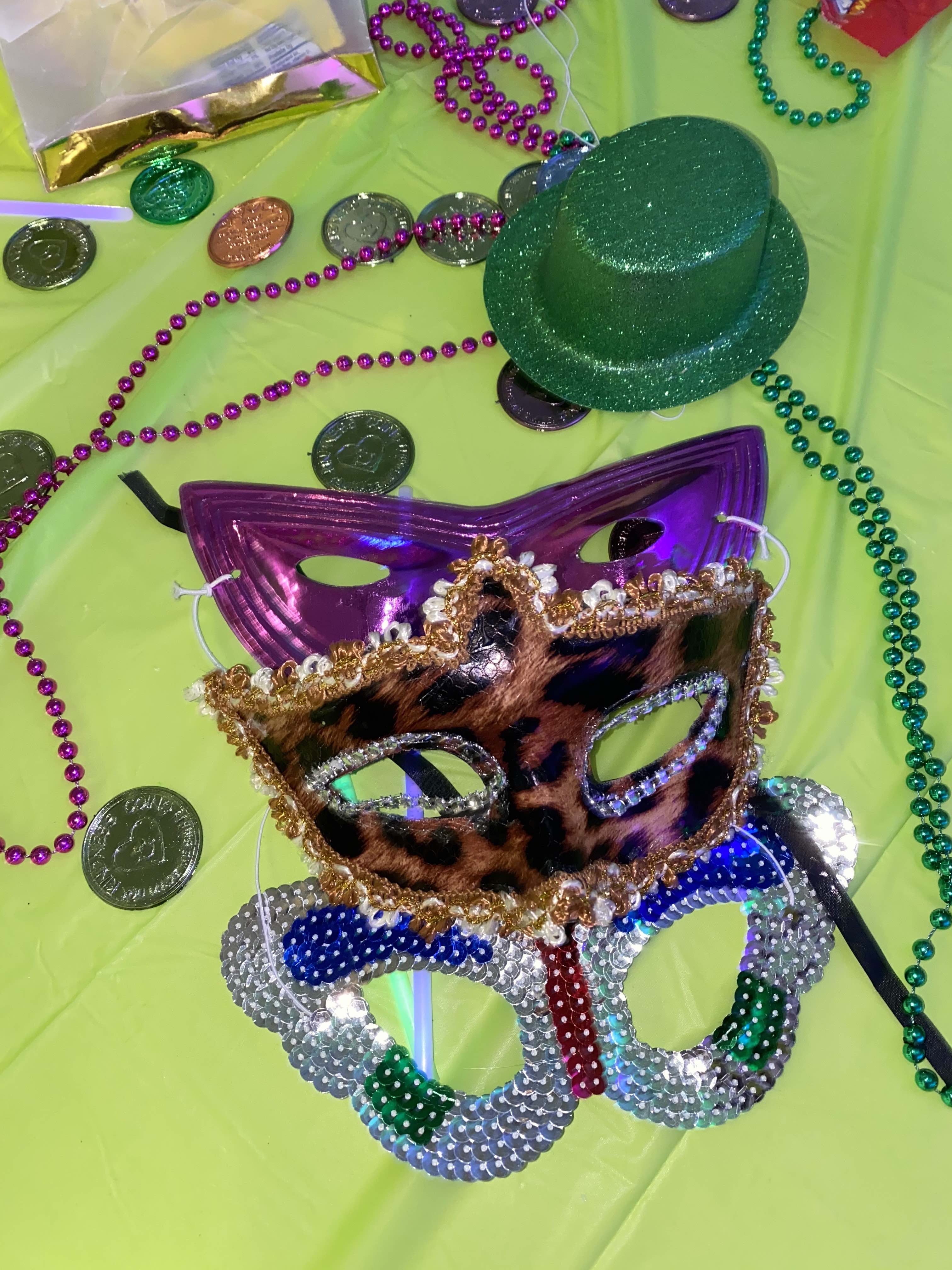 mardi gras masks, beads, coins, and a hat are strewn on a green table