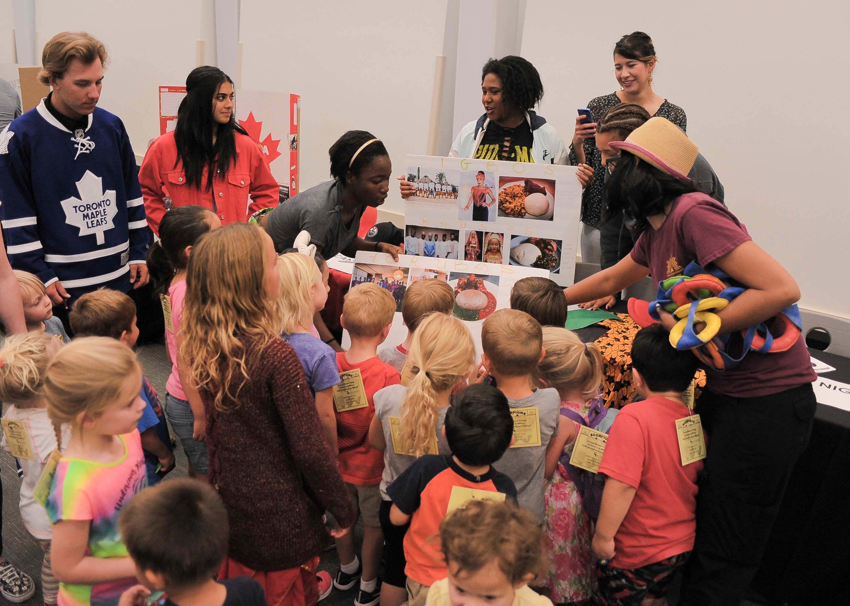 Young children are gathered around a display as AWC students explain various images.