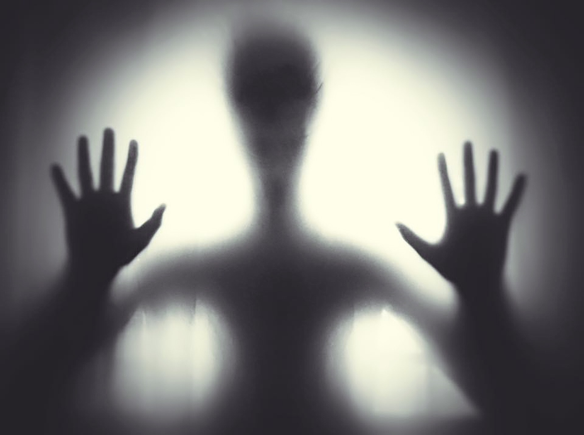 A silhouette of a person with their hands on the screen is illuminated ominously