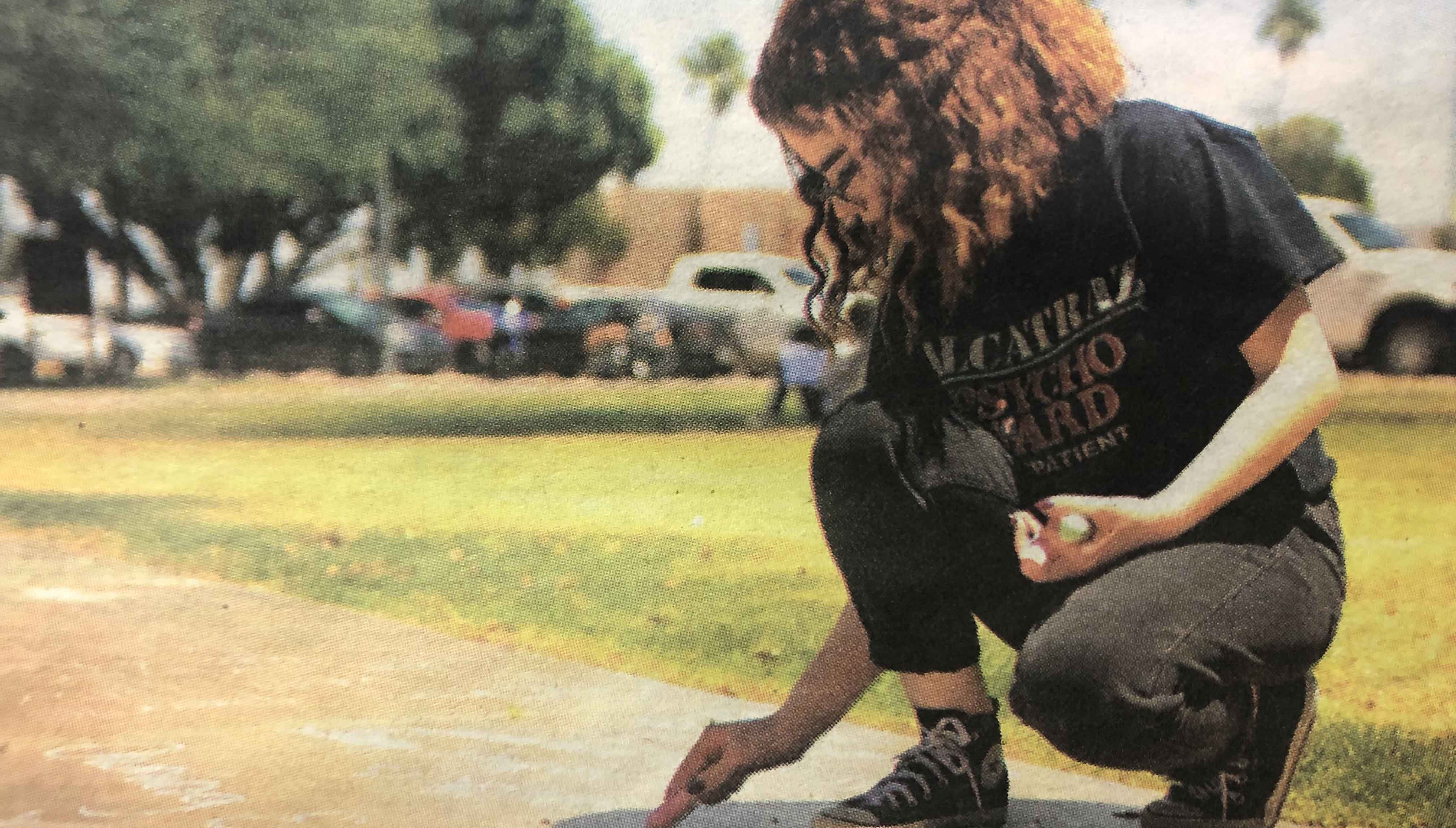 Student kneels down to write with chalk on school sidewalk