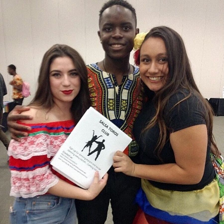 two women and a man pose with a salsa dance booklet