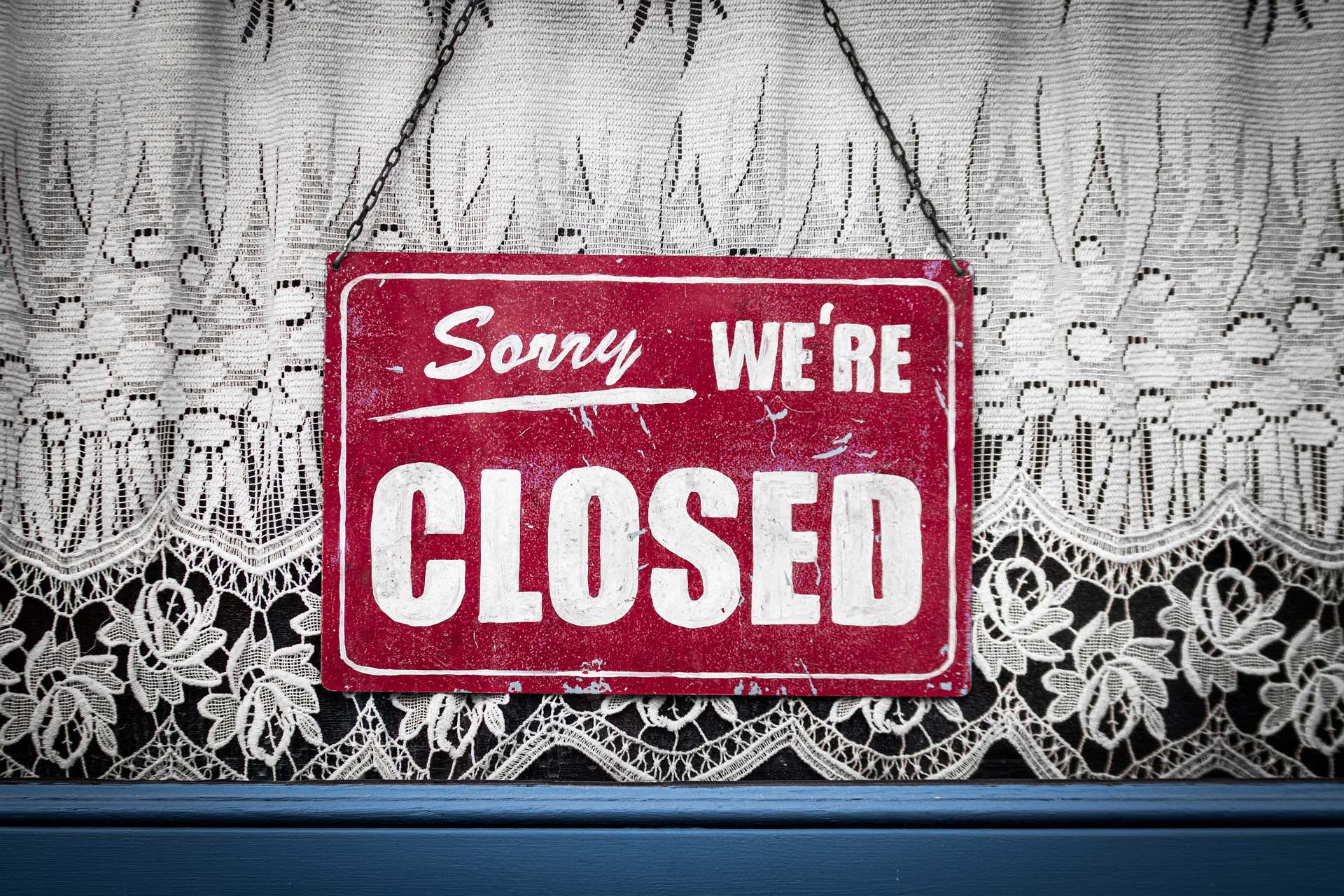 A red "sorry, we're closed sign" is hung in front of a lacy curtain