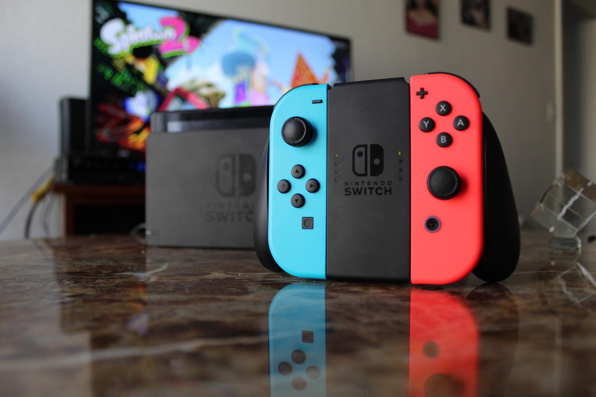 A nintendo switch piece with blue and red sides sits on a dark marble countertop with a video game screen in the background