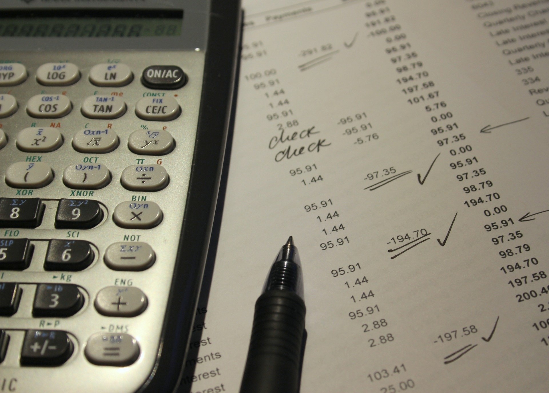 A calculator and pen sit atop a paper used for finance checking 