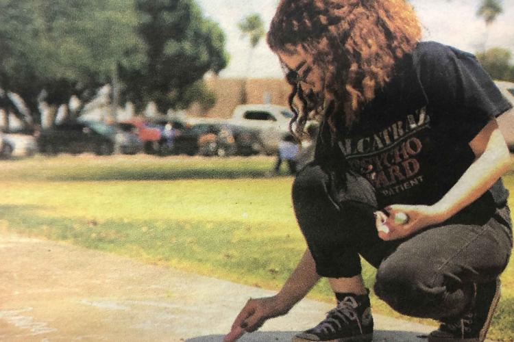 Student kneels down to write with chalk on school sidewalk