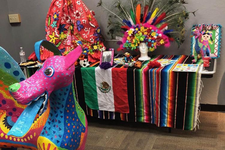 Colorful dog-like sculpture in front of a Mexican heritage display.