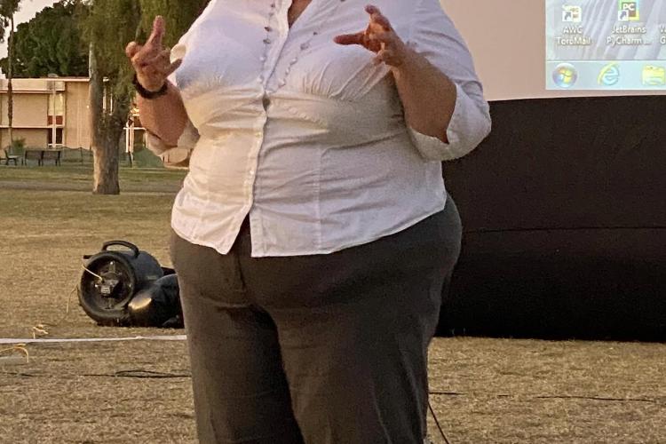 History Professor Monica Ketchum speaks before the screening of the documentary White Wash as part of a week-long focus on Black history at AWC. A blonde woman in a white shirt is speaking outdoors in front of a projection screen.