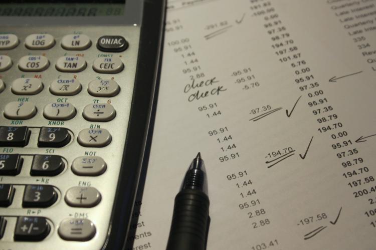 A calculator and pen sit atop a paper used for finance checking 