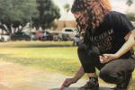 Student kneels down to write with chalk on school sidewalk