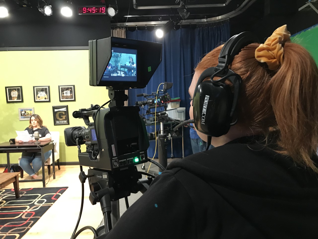 A person stands behind a camera with headphones on, recording the show